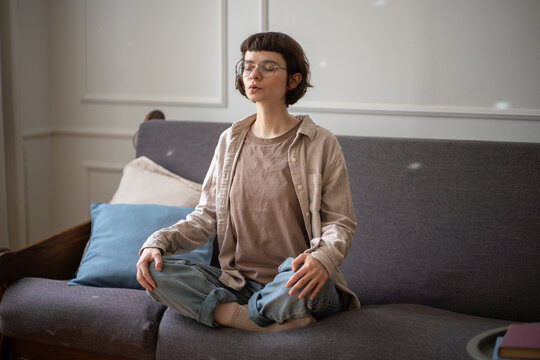 Absorbed woman in cross legged pose on couch inhale and exhale slowly. Female in lotus position do breathing exercises, domestic mindfulness, conscious breath, mental calm, diaphragmatic control