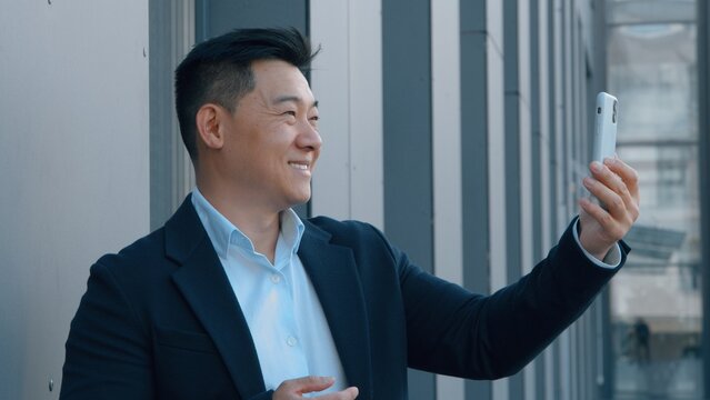 Asian business man talking video call in city with mobile phone chat Korean 40s businessman male talk online internet conference using smartphone Chinese Japanese employer communicate negotiation