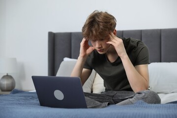 Sad teenage boy with laptop on bed at home