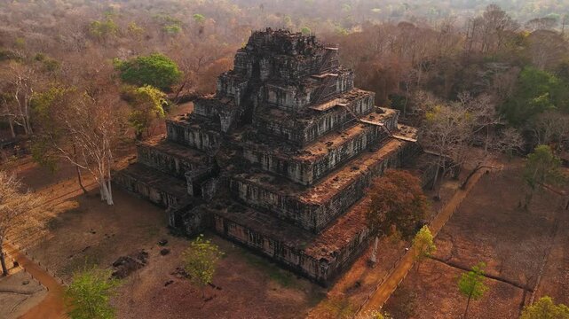 Aerial view of the koh ker temple, a seven tiered pyramid standing amidst the dry cambodian jungle during a hazy morning light.