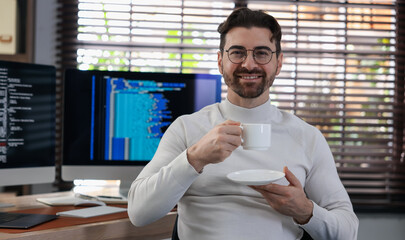 Portrait of smiling programmer in glasses with cup at workplace