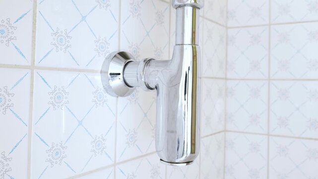 Panning video of a chrome bottle trap installed beneath  bathroom sink. Low, wide angle, close up, real time footage, no people