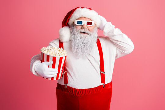 Santa in red suit white beard holds popcorn bucket wear 3D glasses suspenders against pink background Christmas themed promotion