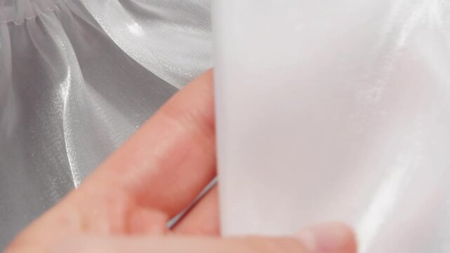 Female hand gently checking glossy satin material creating soft flowing white fabric folds