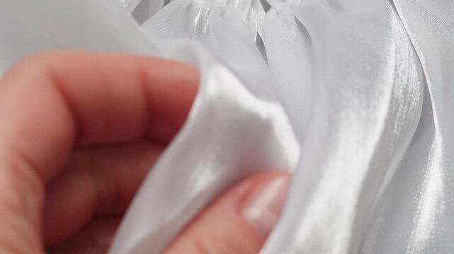 Female hand gently checking glossy satin material creating soft flowing white fabric folds
