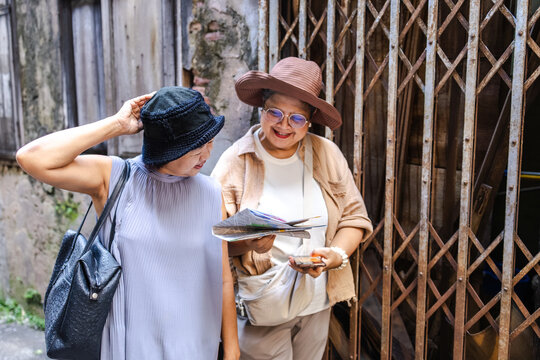 Two senior travelers laugh warmly in a city tour with old school way navigation map, elderly women celebrate retirement carefree holiday journey, aging society lifestyle, pension health insurance - Powered by Adobe