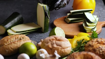 Sliding shot of chef slicing zucchini with lime buns parsley and eggs on surface