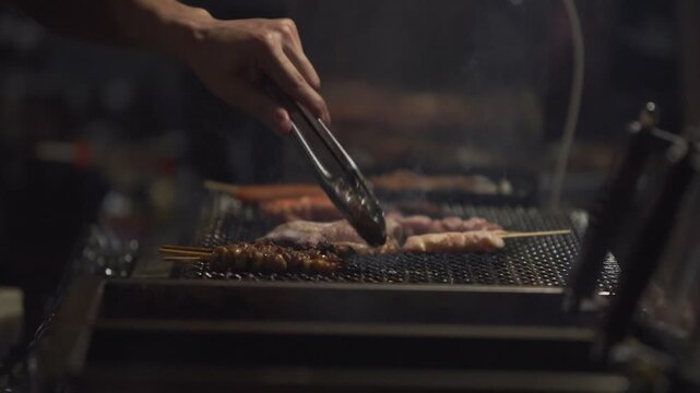 Slow motion showing a street food chef grilling skewers over hot charcoal at a yatai stall in Fukuoka, Japan, with glowing heat and smoke rising in the dark