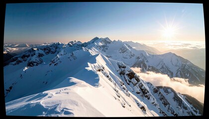 A wide, panoramic view of majestic, snow-covered mountain peaks bathed in the warm glow of the sun, with soft clouds drifting below.