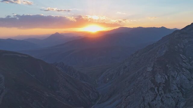 Time-lapse captures the sunset over mountain peaks, with golden light fading into twilight. Strong wind shakes the camera slightly, adding raw motion to the peaceful scene.