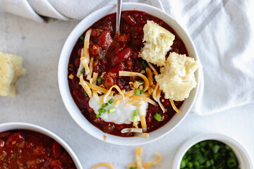 Overhead view of a hearty bowl of chili topped with shredded cheese, sour cream, and sliced green onions.