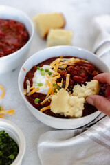 Overhead view of a hearty bowl of chili topped with shredded cheese, sour cream, and sliced green onions.