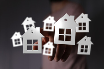 Person's hand with paper home cutouts. Concept of choosing a house, property market, investment, real estate, dream house and future planning.