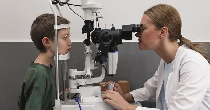 Woman optometrist examining little boy eyes with slit lamp microscope
