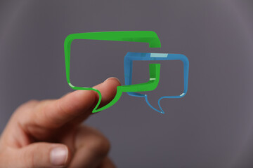 Hand holding green and blue speech bubbles representing communication, discussion, and connection...