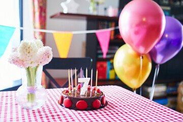 Festive birthday table with a chocolate cake, number seven candle, colorful balloons, flowers, and bunting