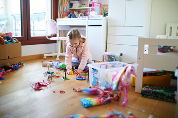 Little girl sitting on the floor in her bedroom and playing with toys