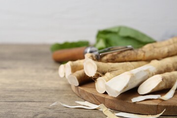 Fresh raw horseradish roots, peeler and leaves on wooden table, closeup. Space for text