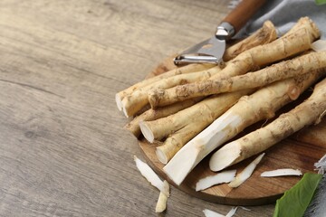 Fresh raw horseradish roots, peeler and leaves on wooden table, closeup. Space for text