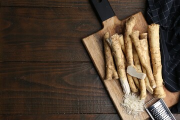 Grated horseradish, grater and fresh roots on wooden table, top view. Space for text