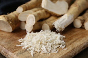 Grated horseradish and fresh roots on wooden table, closeup