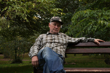 A thoughtful middle-aged gray-haired man in a checkered shirt on a park bench