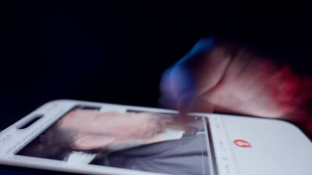 Finger Rapidly Swipes Through Visual Feed on Smartphone Display with Shutter Drag Effect in Red and Blue Light Showing the Whole Life is in the Smartphone and Information Overload