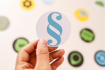Close-up of a hand holding a blue paragraph symbol on a white circle with other colorful circular shapes blurred in the background. Perfect for