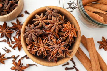 Mulled wine spices. Anise stars in wooden bowl, cloves and cinnamon sticks on white table, top view