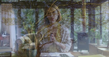 Writing Chinese woman wearing cardigan over blouse at home desk with papers overlaid branches
