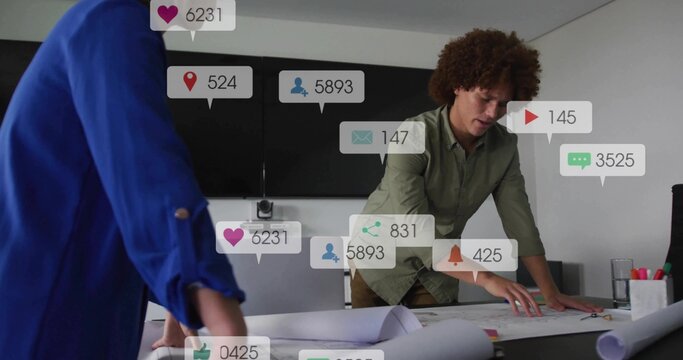 Leaning man in green-shirt examining plans in meeting room with blue-blazer peer and social icons