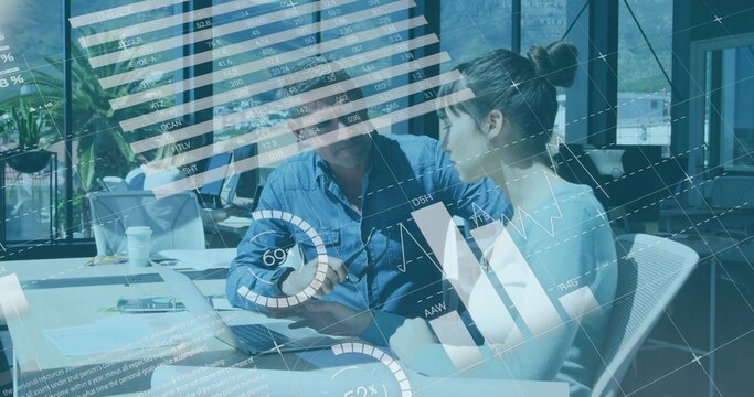 Man in blue shirt and woman in sweater reviewing laptop at meeting table with documents