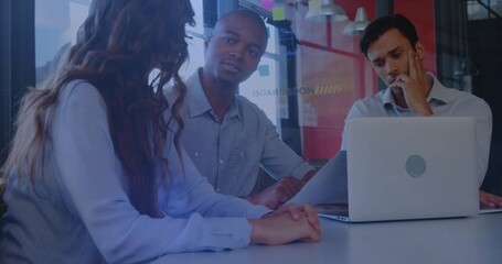 Discussing woman in light-blue blouse with colleagues in glass boardroom using laptop and papers