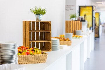 Buffet with fresh fruit in the foreground. Plates, some plants, and wooden boxes as decoration cab be seen in the background in a bright and natural setting.