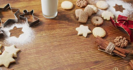 Showing assorted holiday cookies and cookie cutters on kitchen tabletop with milk, sugar, cinnamon
