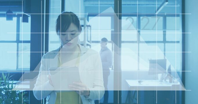 Holding foreground Asian woman wearing blazer reading tablet in open office with data overlay