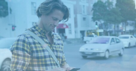Standing man wearing yellow-plaid shirt, looking at phone at city corner, with crossbody bag, cars