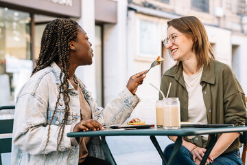 Multiethnic women partners sharing food during outdoor brunch