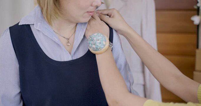 Asian young dressmaker measuring designer&rsquo;s shoulder with precision tape for customized clothing in handmade apparel business, working in fashion studio filled with samples and textile equipment