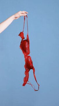 Hand of woman holding red lace bra and dropping it. Braless concept as vertical video for social media.