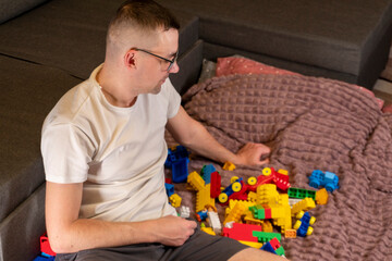 Young man sitting and playing with a children's construction set