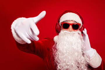 Santa in red costume with hat beard and headphones points forward in festive holiday portrait red...