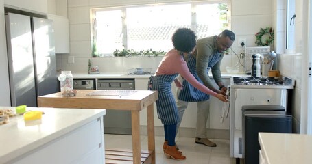African American couple in kitchen opening oven removing tray onto island, discussing dish - Powered by Adobe