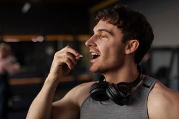 Sports multivitamins. Young European man taking supplement capsule, eating omega 3 or amino acid...