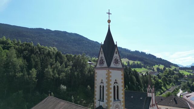 church steeple detail in austria near brenner pass scenic small town in the alps with mountain background river train tracks alpine village christian cross top colorful white drone footage scene 