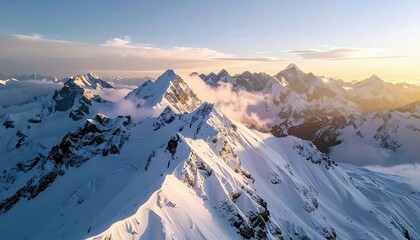 An aerial view of a vast, snow-covered mountain range at sunrise, with dramatic peaks and clouds.