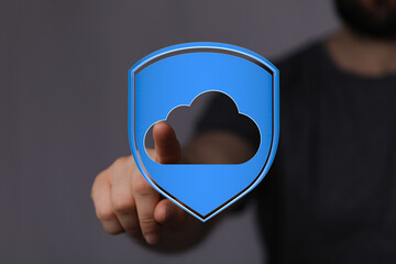 Man's finger touching a blue cloud shield icon, symbolizing secure data storage and information technology.