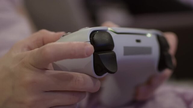 Child playing video game at home, close-up of small hands holding controller, finger pressing trigger during focused gaming session