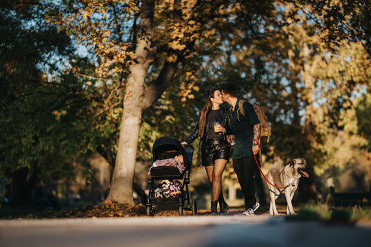 A couple shares a kiss during a gentle stroll through a sunlit autumn park while pushing a stroller and walking their dog. This warm, candid scene captures love, family, and everyday life.