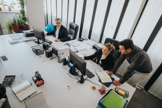 Professional office environment showcasing teamwork between diverse colleagues collaborating on a project, utilizing digital tools, and analyzing documents. - Powered by Adobe